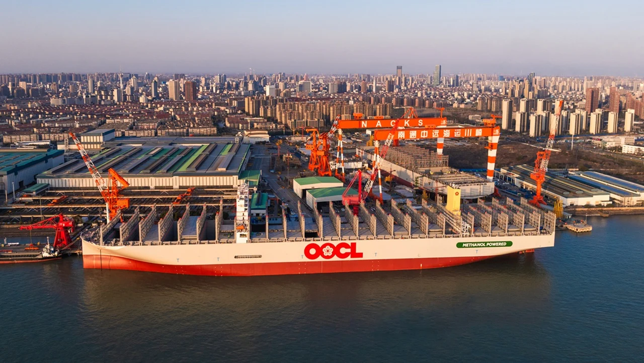 The image shows an OOCL container ship docked at a shipyard during construction/outfitting, directly relevant to the article discussing container line capacity growth and new ship deliveries.