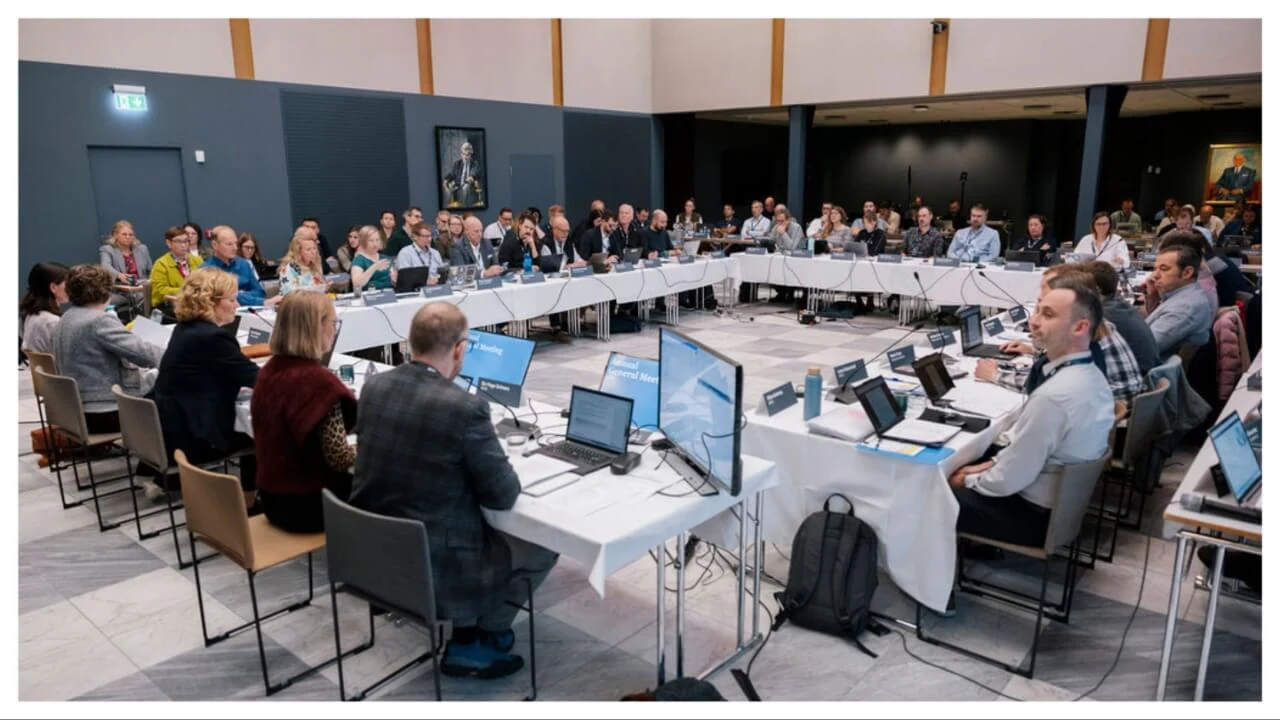 A real photograph showing participants seated around tables during the AECO Annual General Meeting, directly corresponding to the article discussing the event in Oslo.