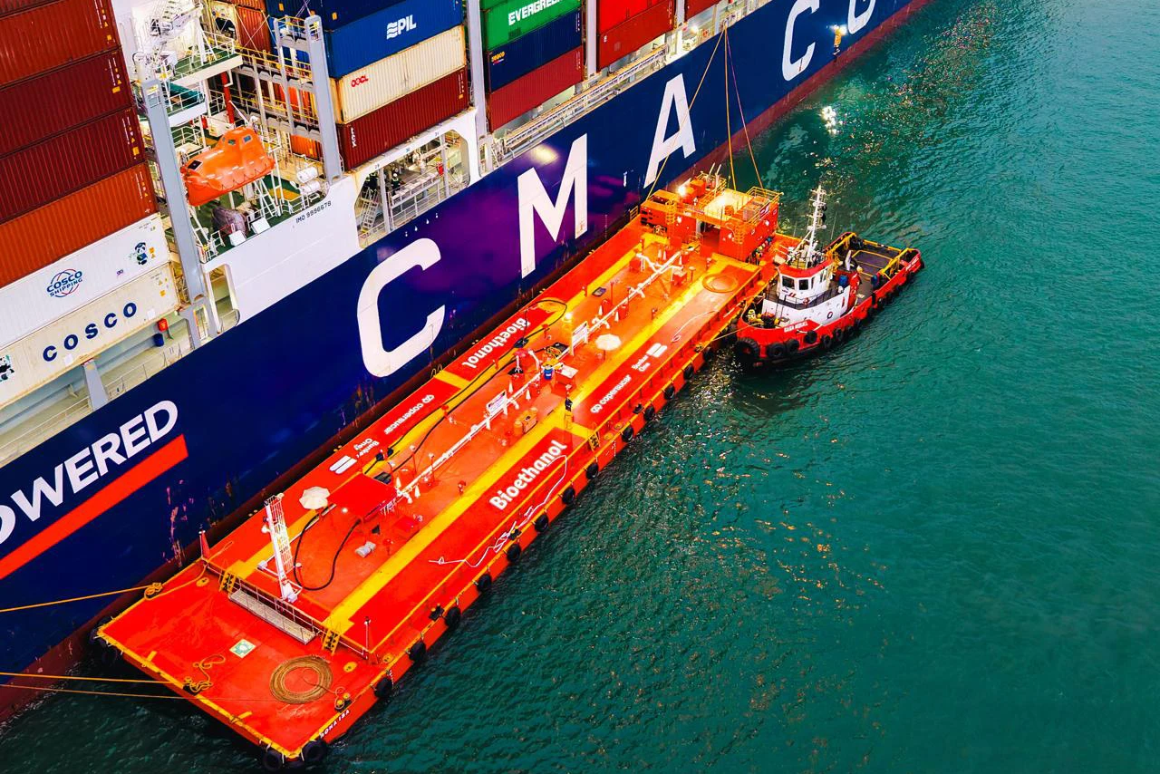 Real aerial photograph showing a bioethanol bunkering barge marked 'Bioethanol' alongside a CMA CGM container ship during a refuel operation, directly relevant to the article.