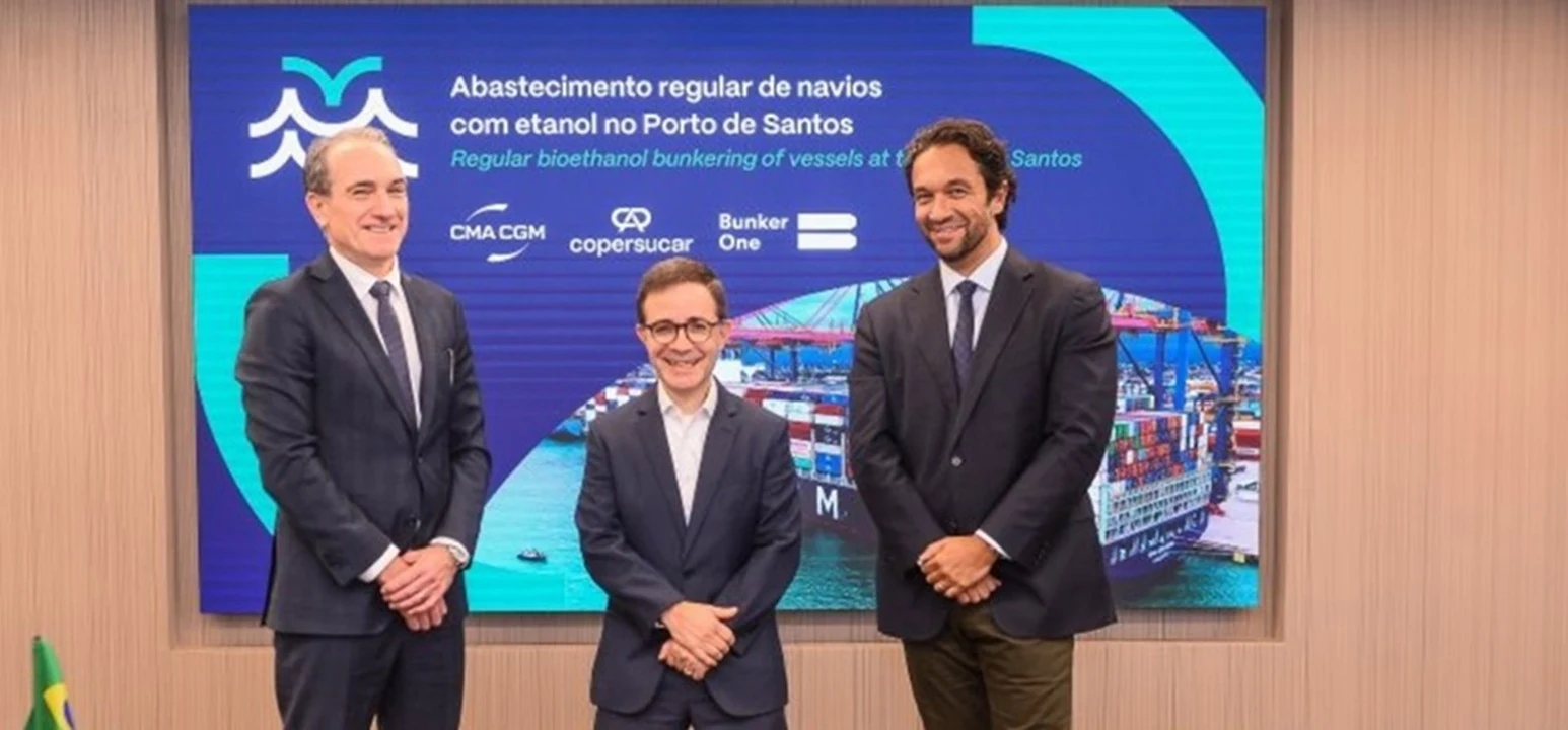 Real news photo showing corporate and port executives posing in front of a presentation screen announcing regular bioethanol bunkering at the Port of Santos, featuring logos of CMA CGM, Copersucar, and Bunker One.